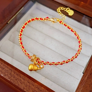 Détail d'un bracelet en corde rouge et chaîne dorée avec pendentif calebasse et cristaux