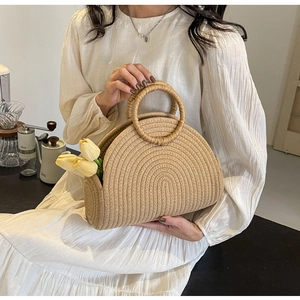 Detail view of beige half-moon straw handbag with round handle and decorative flowers