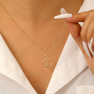 Dettaglio della collana con pendente a pretzel dorato e zirconi su camicia bianca