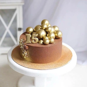 Detailed view of chocolate cake decorated with various gold balls and number 15 topper