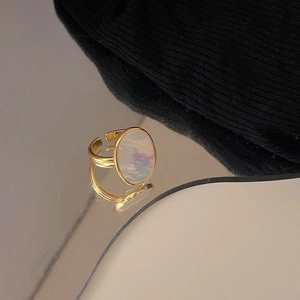 Close-up of a gold vintage oval ring with a white shell inlay on a reflective surface