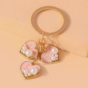 Detail of gold metal keychain with pink enamel hearts and pearl embellishments