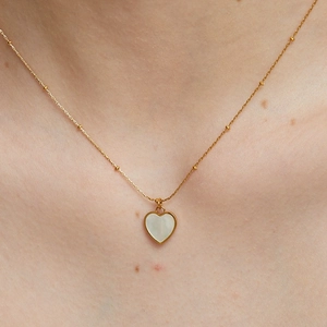 Elegant gold chain necklace with white mother of pearl heart pendant on woman neck