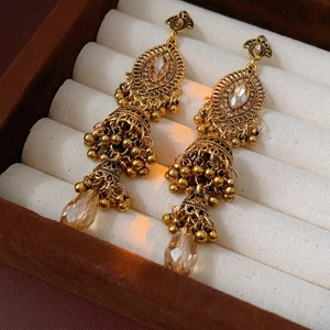 Boucles d'oreilles Jhumka dorées avec pompons en cristal champagne dans un écrin