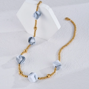 Bohemian gold beaded necklace with marble cube pendants on white stone display