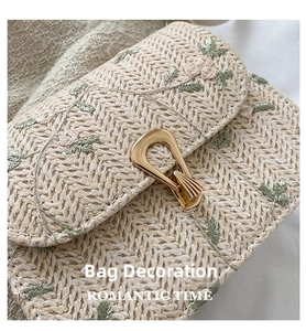 Close-up of floral embroidery and golden metal buckle on straw crossbody bag