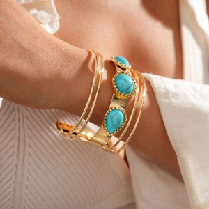 Detail of layered gold metal bracelet set featuring three pear-shaped turquoise stones