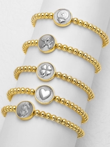 Detail of 18k gold plated beaded bracelets with heart and clover pendants on white stand