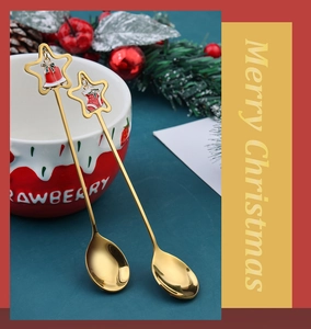 Detail of gold Christmas spoons with festive charms next to a strawberry ceramic cup