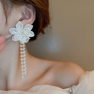 Dettaglio di orecchini a fiore bianco con lunghe nappe di perle finte su una modella
