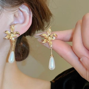 Elegant gold flower earrings with white water drop pearls shown on a model