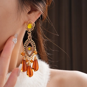 Close-up of vintage gold tassel earrings with amber stones and crystals worn by a model