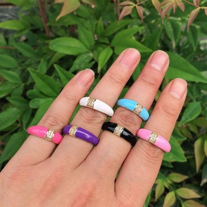 Close-up of six colorful enamel rings with inset zircon on a hand in natural light