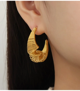 Vue détaillée de grandes boucles d'oreilles spirales dorées avec texture tissée sur modèle
