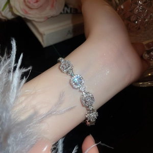Detail of silver geometric bracelet with white crystals on a model's wrist with feathers