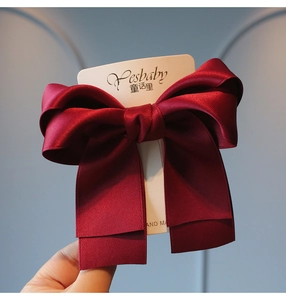 Close-up of a large wine red satin ribbon bow hair clip on a display card