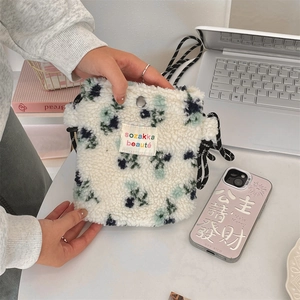 Detail of plush floral crossbody bag with metal snap button and woven label on desk