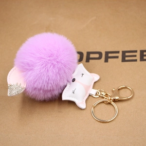 Close-up of purple plush fox keychain with golden lobster clasp and faux fur ball charm