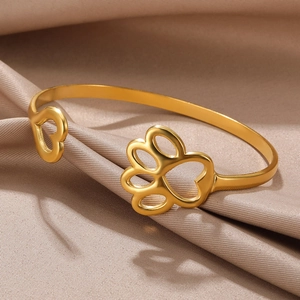 Detail of gold open bangle featuring hollow heart and cat paw prints on silk background