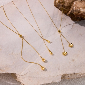 Close-up of gold Y-chain necklaces with sphere, teardrop, and heart pendants on stone