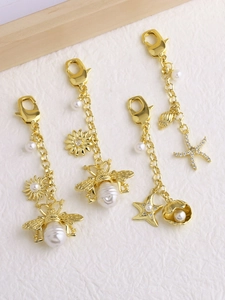 Détail de breloques abeille et étoile de mer dorées avec perles et strass scintillants
