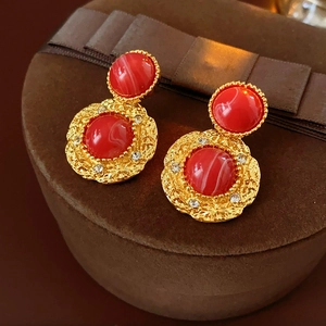 Dettaglio di orecchini vintage rossi con finitura dorata martellata e strass brillanti