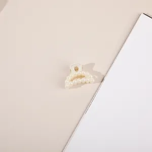 Detail of a semi-circular pearl mini hair claw clip with cream finish and metal spring