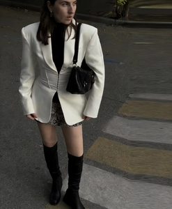 Street style view of a white cinched waist blazer paired with floral skirt and over-knee boots