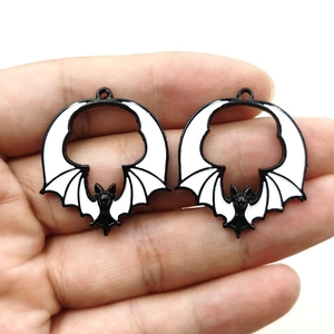 Detail of bat-shaped enamel charms in black and white shown on hand for size reference