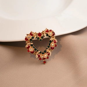 Close-up of heart floral brooch with red and green gemstones on golden alloy
