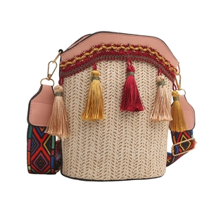 Detail of woven straw bucket bag with pink leather trim and colorful geometric strap