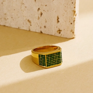 Close-up of gold-plated titanium ring with green pavé set crystals on stone texture