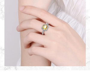 Detail shot of a silver halo ring featuring a square cushion cut yellow gemstone on a finger