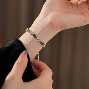 Detail of silver chain bracelet with oval green gemstone and flower-shaped zircon on wrist