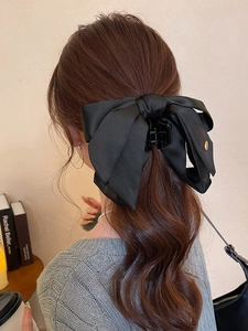 Detail of elegant black satin bow hair claw with gold logo emblem on a ponytail