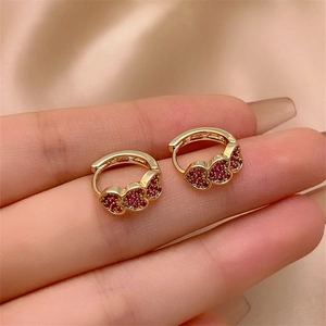 Handheld close-up of gold heart earrings with red zircon stones and click-top clasp