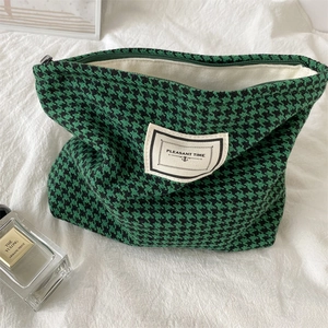 Detail of green houndstooth makeup bag with woven label on soft white fabric