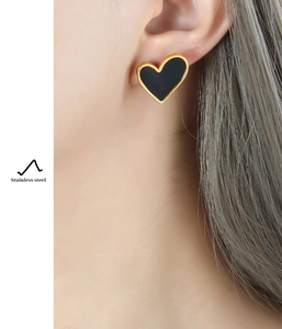 Close-up of heart-shaped stainless steel earrings in black and gold on model