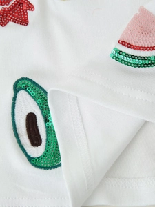Detailed close-up of sequined watermelon and avocado embroidery on white knit fabric
