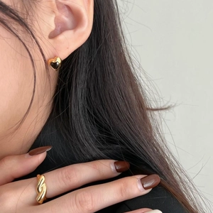 Close-up of model wearing gold heart earrings and textured wave ring in a chic setting