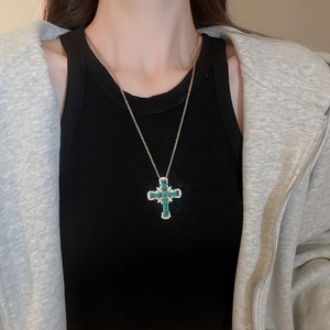 Gros plan d'un collier pendentif croix dorée avec pierres vertes sur le cou d'un modèle