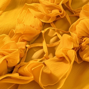 Macro shot of yellow chiffon fabric featuring ruffled edges and delicate woven tie details