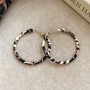 Close-up of leopard print hoop earrings with golden metal clasps and textured fabric wrap
