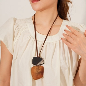 Detail of a long necklace featuring irregular amber and dark stone pendants on a beige shirt