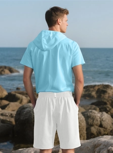 Rear view of a man wearing a blue linen hooded t-shirt and white shorts at the beach