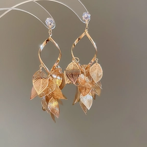 Detail view of golden leaf tassel earrings with sparkling crystals on a minimalist stand