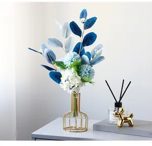 Detail of blue faux eucalyptus and spherical flowers in a gold geometric glass vase