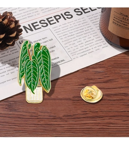 Detail of green potted plant enamel pin with golden metal edges on a wooden table