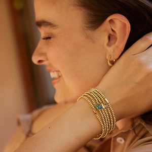 Close-up of gold beaded birthstone bracelets and twisted hoop earrings on female model