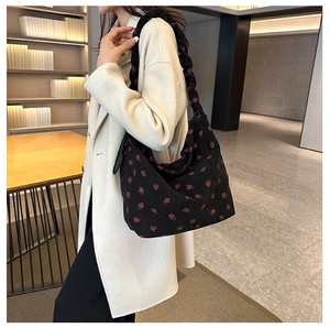 Close-up of black corduroy shoulder bag featuring red strawberry print and ruched strap